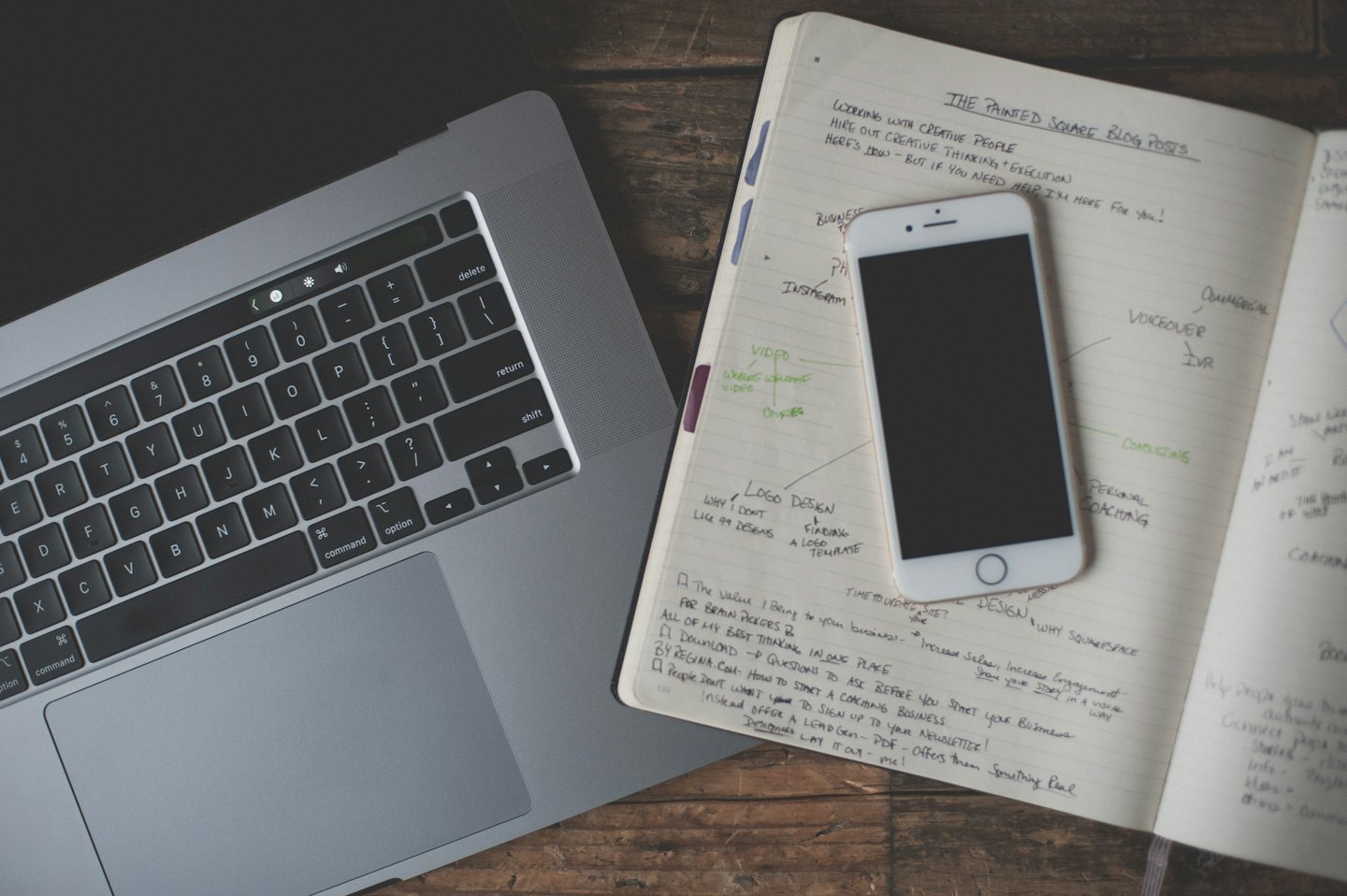 Silver laptop and notebook with handwritten notes on a wooden desk.