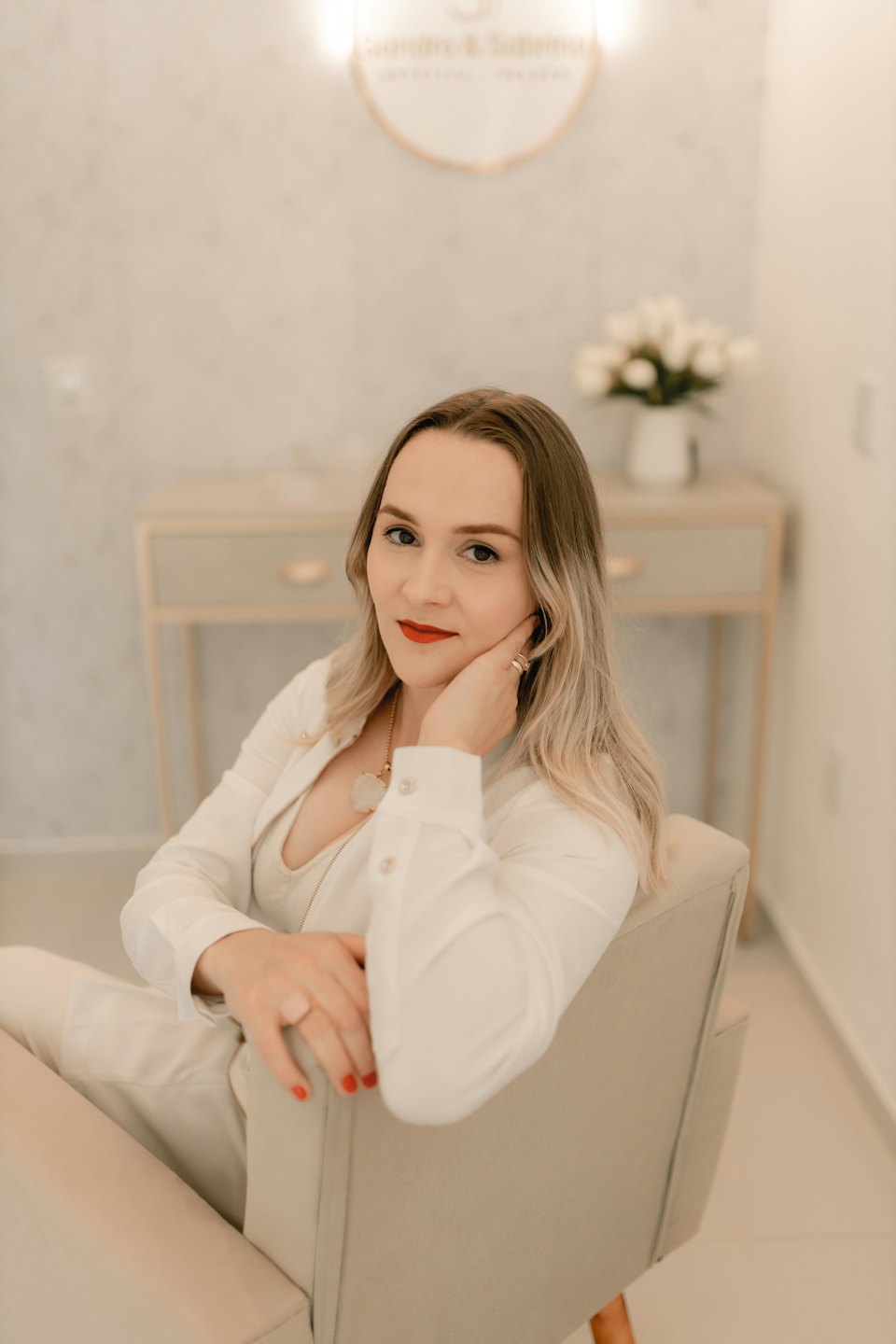 Woman in a suit sitting in an armchair with her hand resting on her cheek.